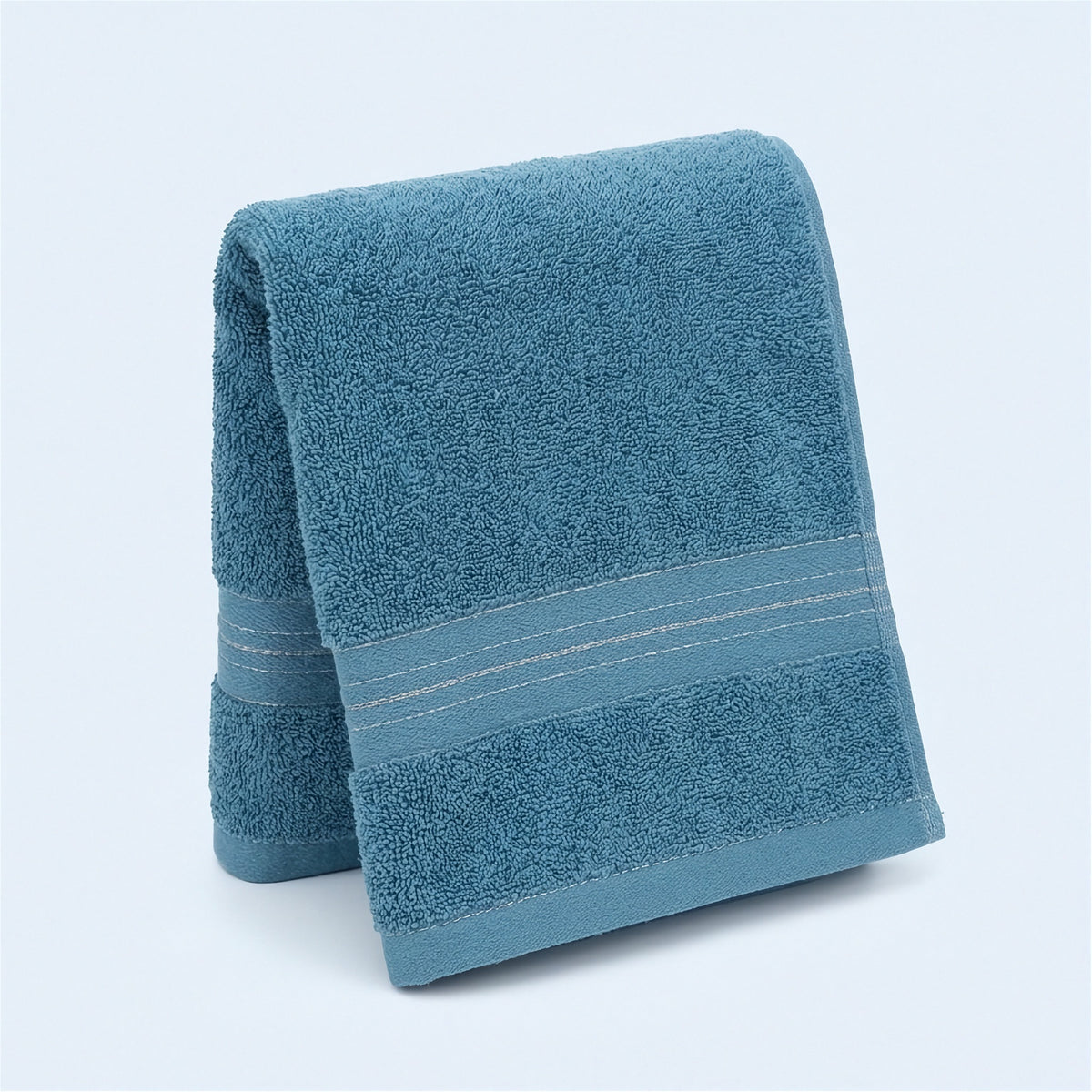 A folded teal terry towel with a woven striped border stands upright against a pale background.