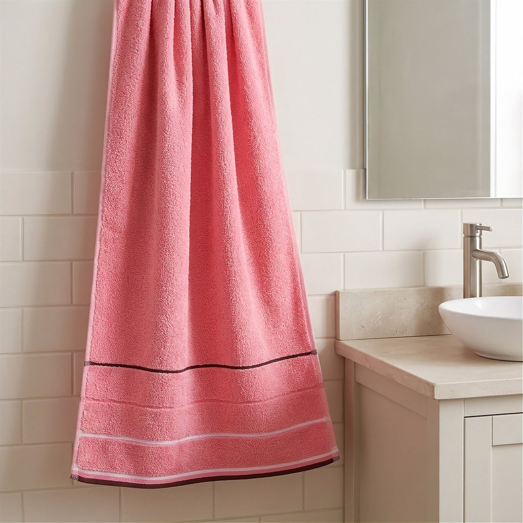 A pink terry towel with brown and white stripes hangs beside a white bathroom sink against white tiles.