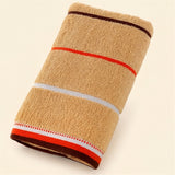 A folded tan terry towel with brown, orange, and white stripes rests diagonally on a cream background.