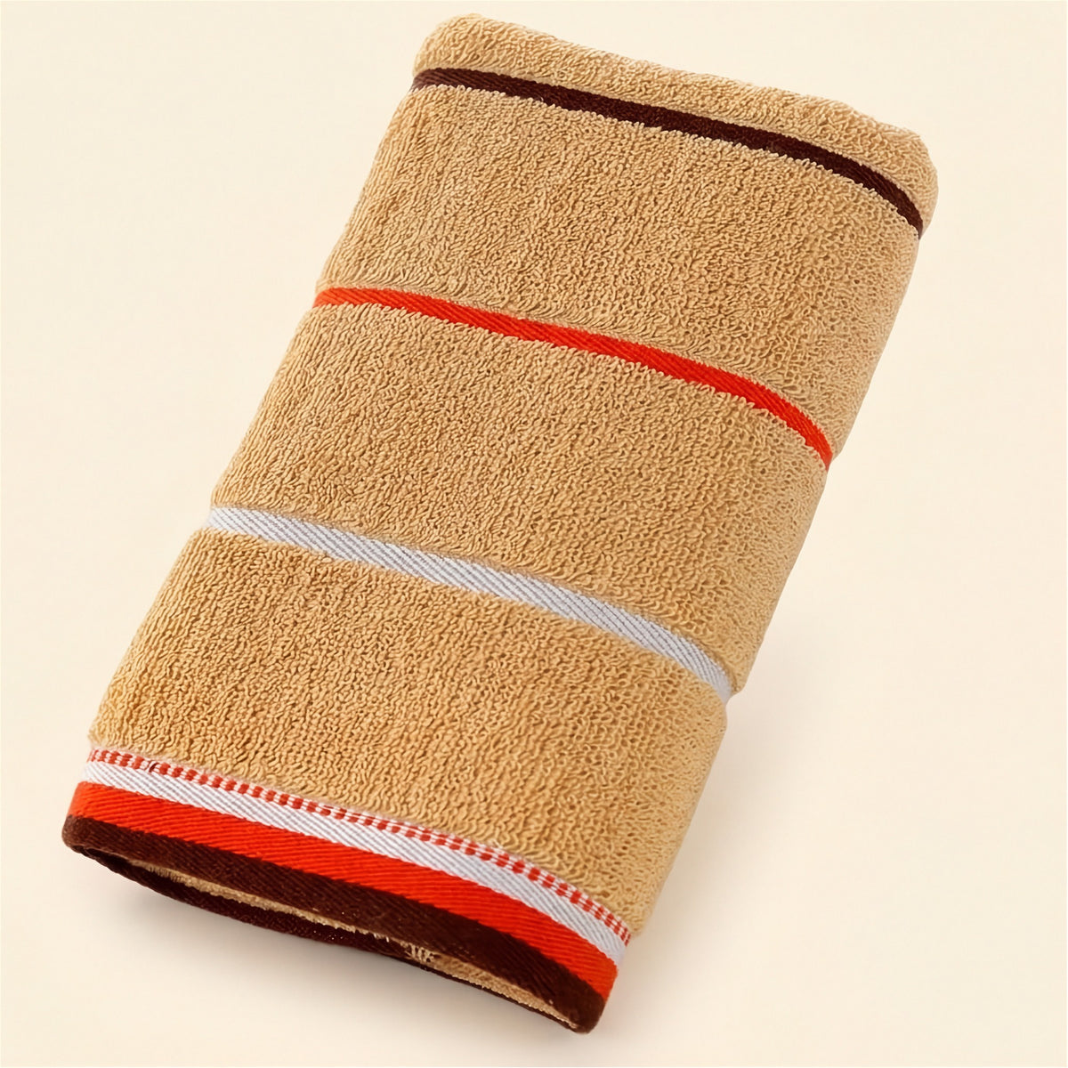 A folded tan terry towel with brown, orange, and white stripes rests diagonally on a cream background.