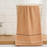 A tan terry towel with brown, peach, and white stripes hangs over a gold wire basket on a wooden bathroom counter.