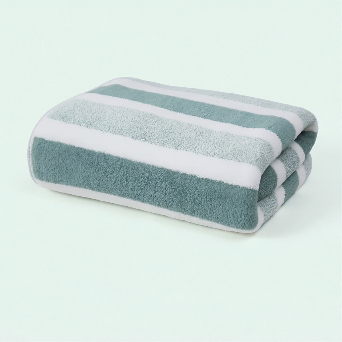 A folded towel with broad muted green, light gray, and white stripes rests on a pale mint background.