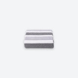 A neatly folded terry towel with broad gray and white stripes sits centered on a light gray background.