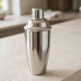 A polished stainless steel cocktail shaker standing on a light stone countertop with a softly blurred kitchen background.