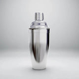 A polished silver cocktail shaker with a domed lid and grooved cap stands upright against a light gray background.