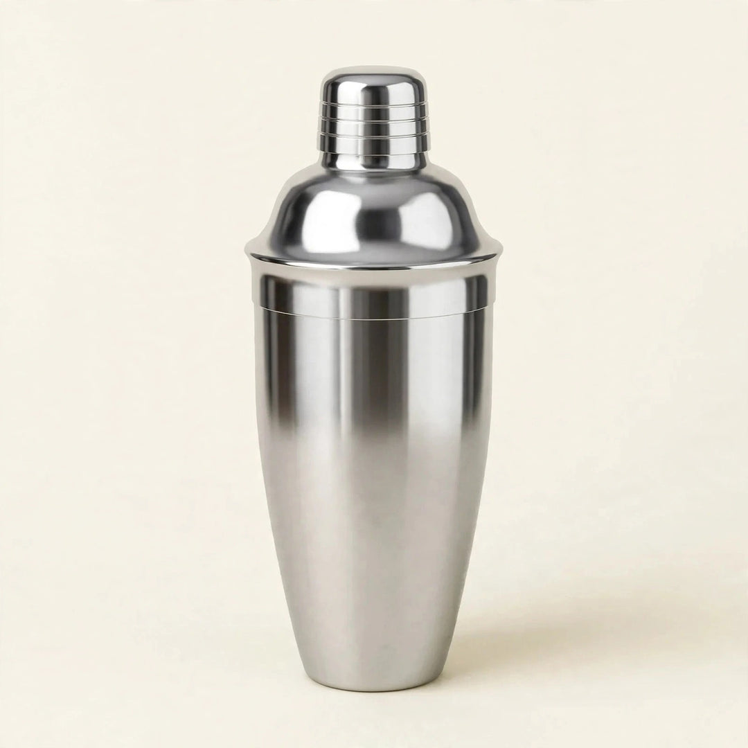 Silver metal cocktail shaker with a domed lid and ridged cap stands upright against a cream background.