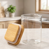An open clear glass jar stands beside its bamboo lid with a white sealing ring on a light kitchen countertop.