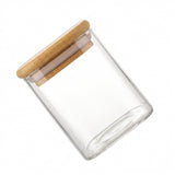 An empty clear glass jar with a bamboo lid and white sealing ring is tilted diagonally against a white background.