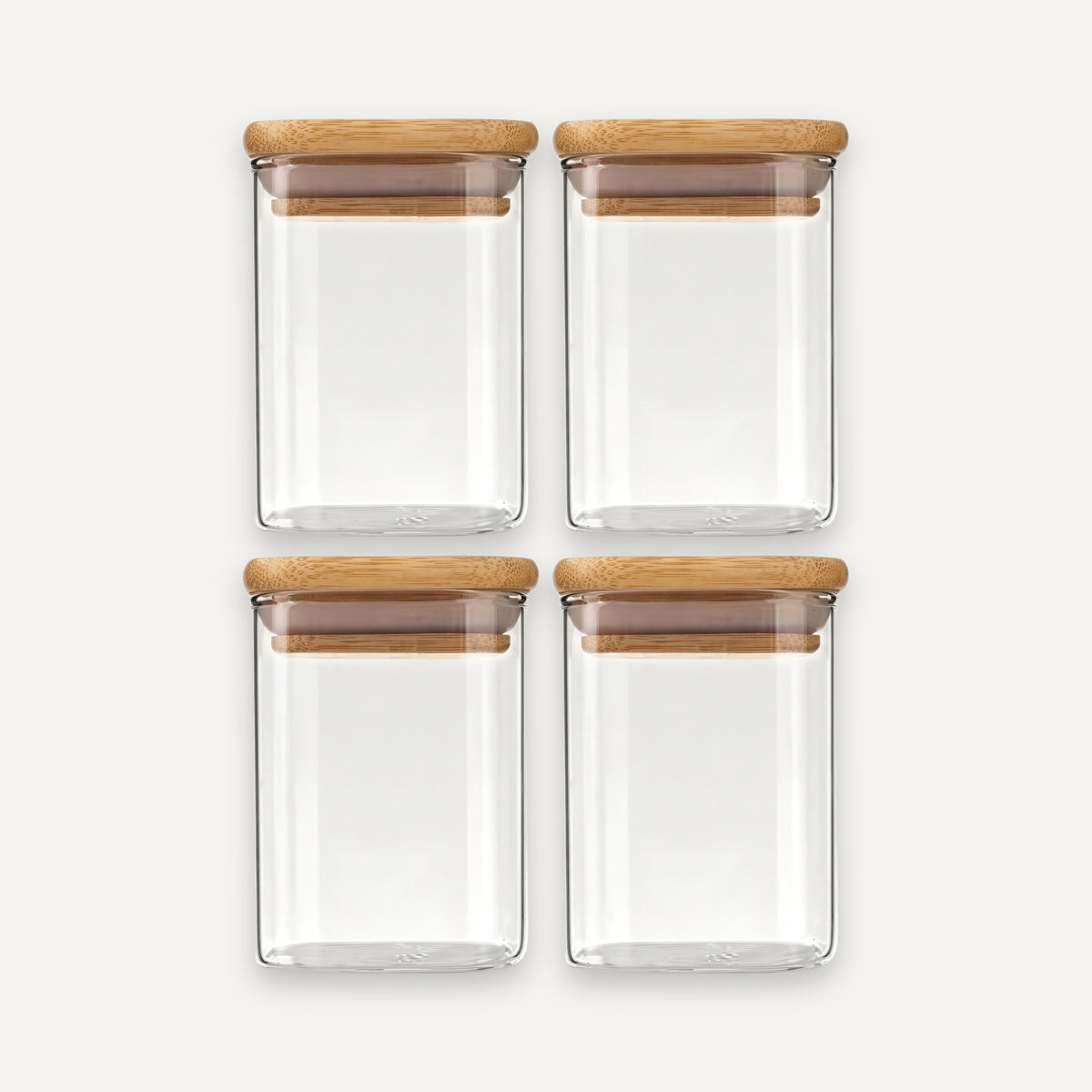 Four empty clear glass jars with bamboo lids are arranged in two rows of two against an off-white background.