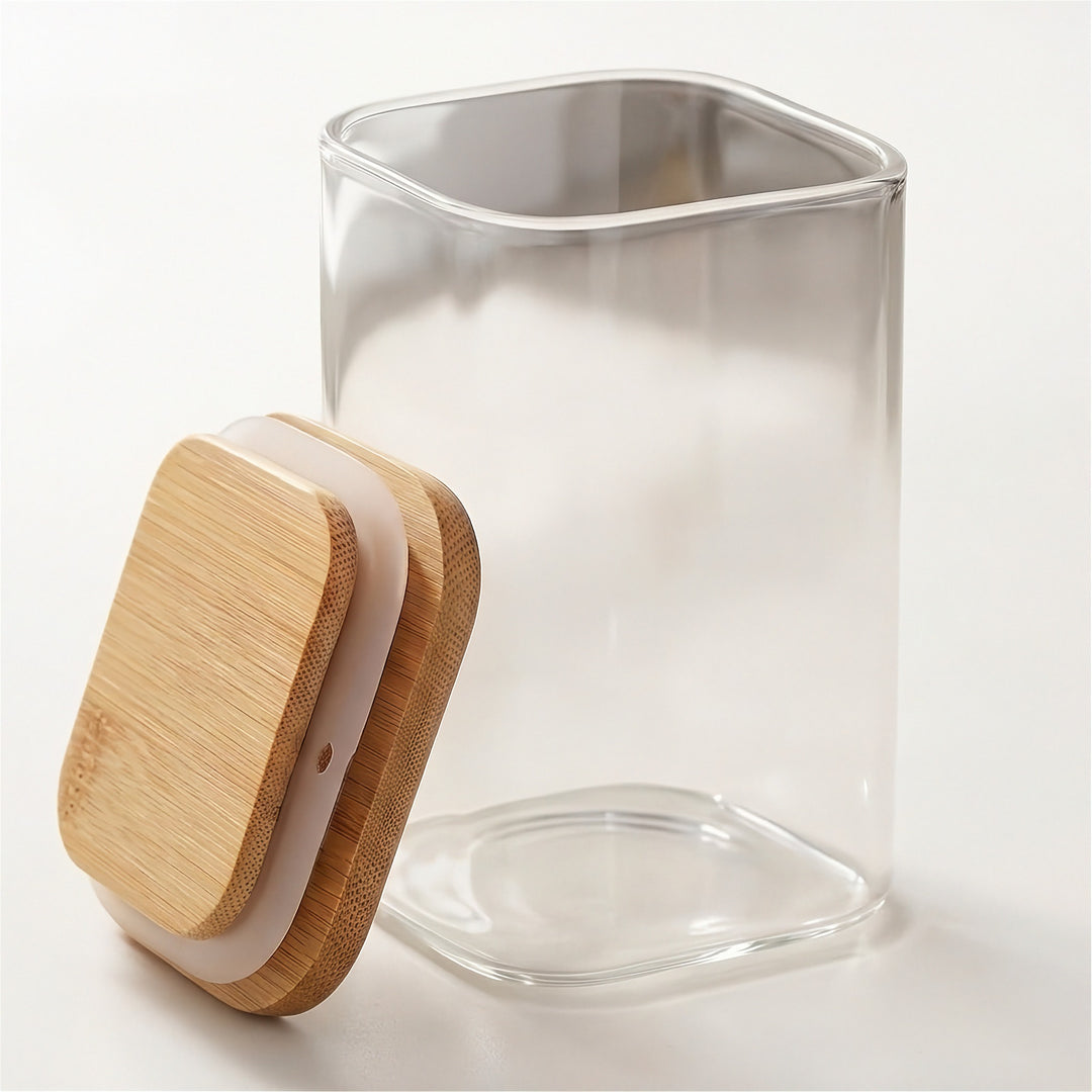 An open clear glass jar stands on a white surface with its bamboo lid leaning beside it, revealing a white sealing ring.