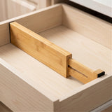 A natural bamboo drawer divider with an extended sliding section and black end pads spans an empty cream drawer.