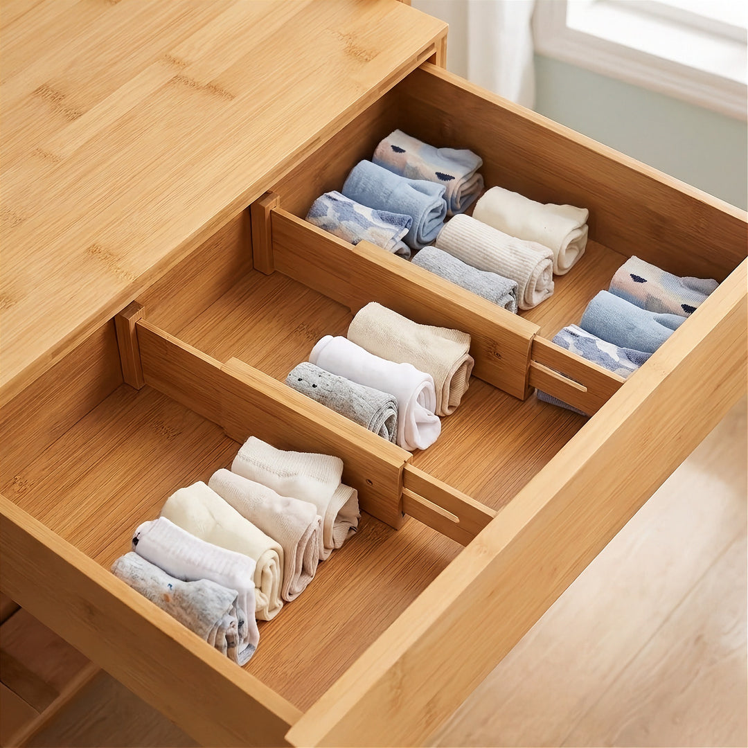 Two natural bamboo dividers separate rolled white, grey, and pale blue socks into sections inside an open wooden drawer.