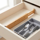 A light brown bamboo divider spans an open cream drawer beside a gray cutlery tray holding a silver spoon and fork.