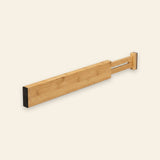 A natural bamboo drawer divider with black end pads and an extended slotted section lies diagonally against a cream background.