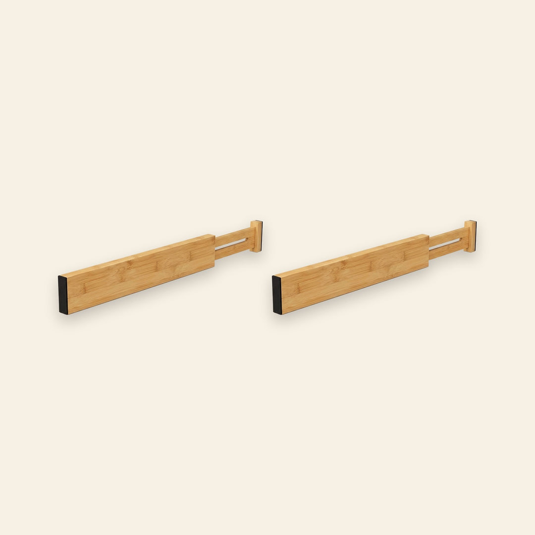 Two light brown bamboo drawer dividers with extendable slotted ends and black end pads sit side by side against a cream background.