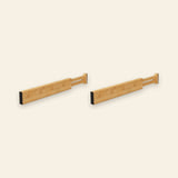 Two light brown bamboo drawer dividers with extendable slotted ends and black end pads sit side by side against a cream background.