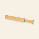 One natural bamboo drawer divider with an extended slotted section and black end pads sits against a cream background.