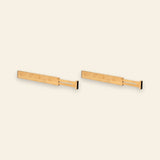 Two natural bamboo drawer dividers with extended slotted sections and black end pads sit side by side against a cream background.