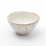 A small ceramic bowl with a matte off-white glaze, featuring a subtle lotus petal design molded into the exterior and a rustic brown rim, set against a plain white background.