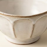 Close-up of a ceramic bowl with a textured, off-white glaze and a rustic brown rim, showing the interior design and handcrafted details.