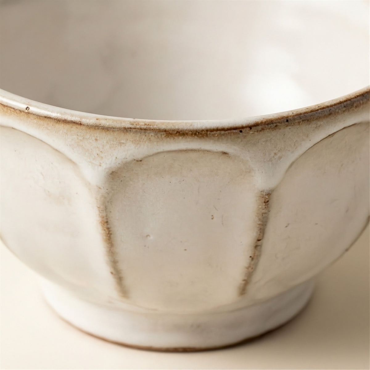 Close-up of a ceramic bowl with a textured, off-white glaze and a rustic brown rim, showing the interior design and handcrafted details.