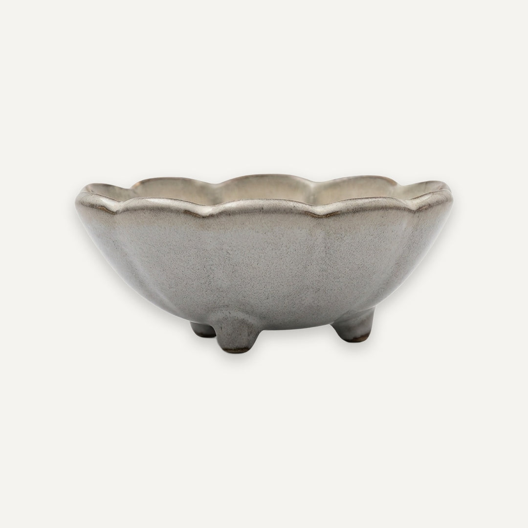 A small ceramic bowl with a scalloped rim and three short feet, shown on a plain light background.