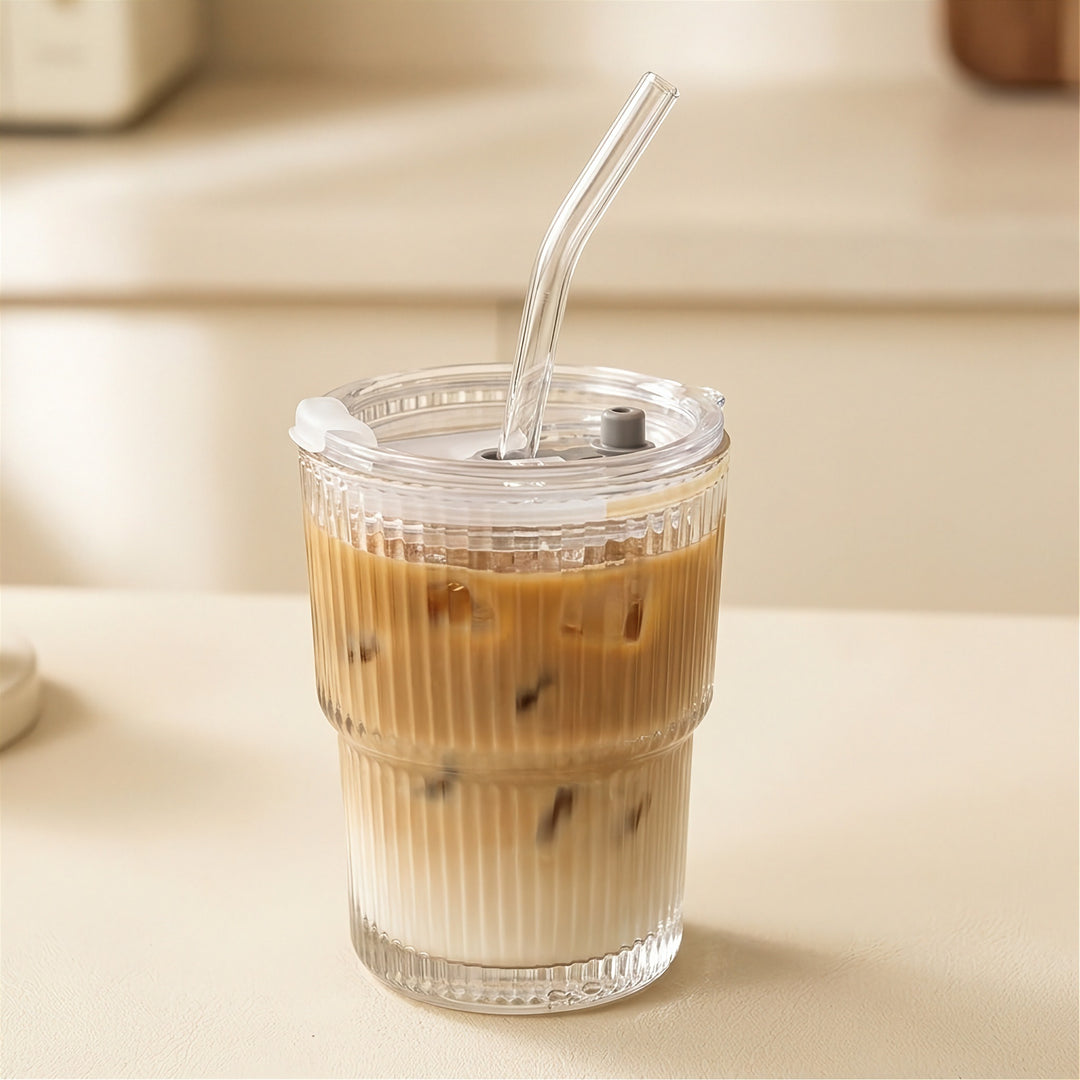 Clear ribbed tumbler with a transparent lid and bent straw holds layered iced coffee on a cream counter against a blurred kitchen background.