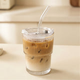Clear ribbed tumbler with a transparent lid and bent straw holds layered iced coffee on a cream counter against a blurred kitchen background.