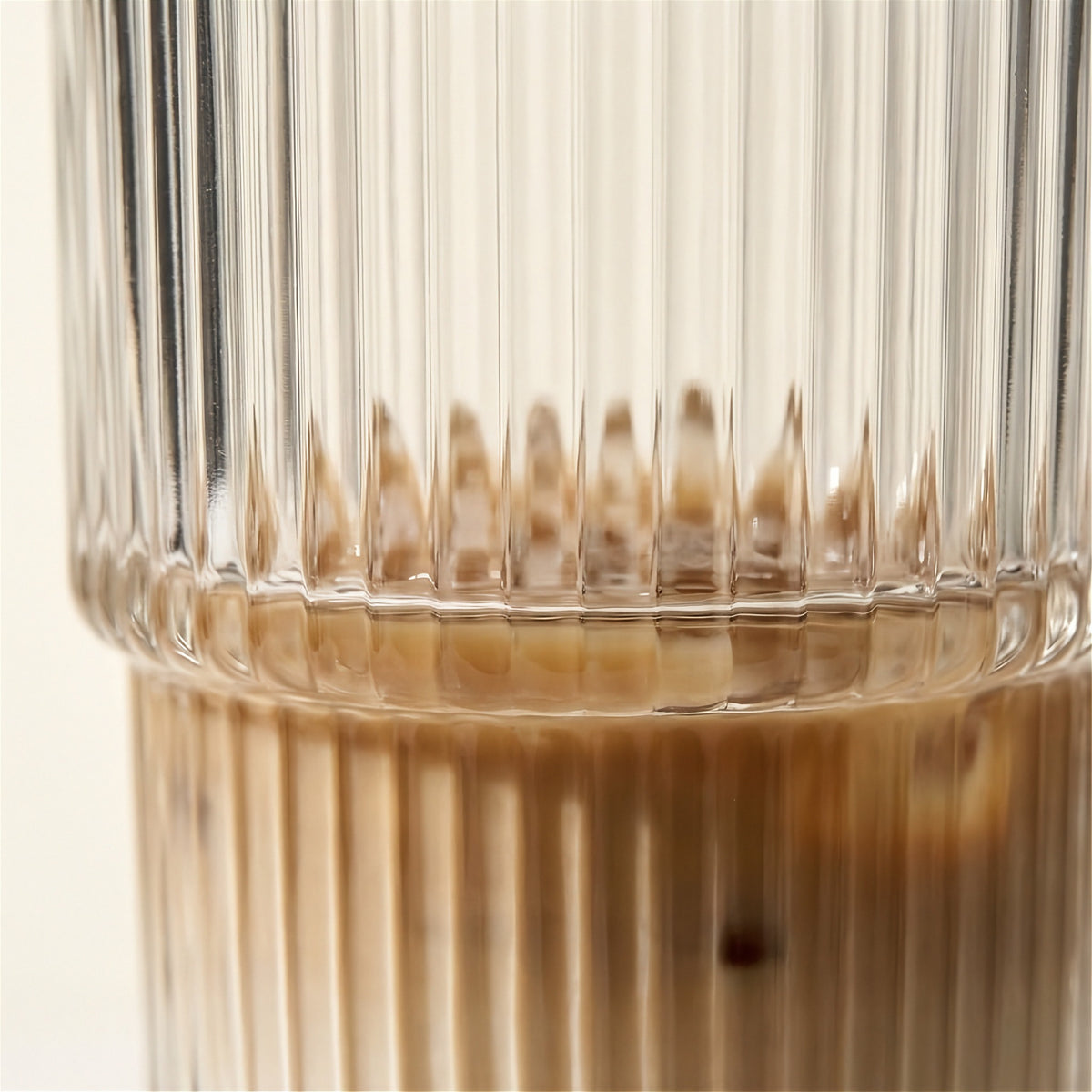 Close-up of a clear tumbler shows vertical ribs and a stepped middle with brown coffee visible through the lower section.