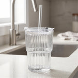 Empty clear ribbed tumbler with a transparent lid and straight straw stands on a light kitchen counter beside a sink and faucet.