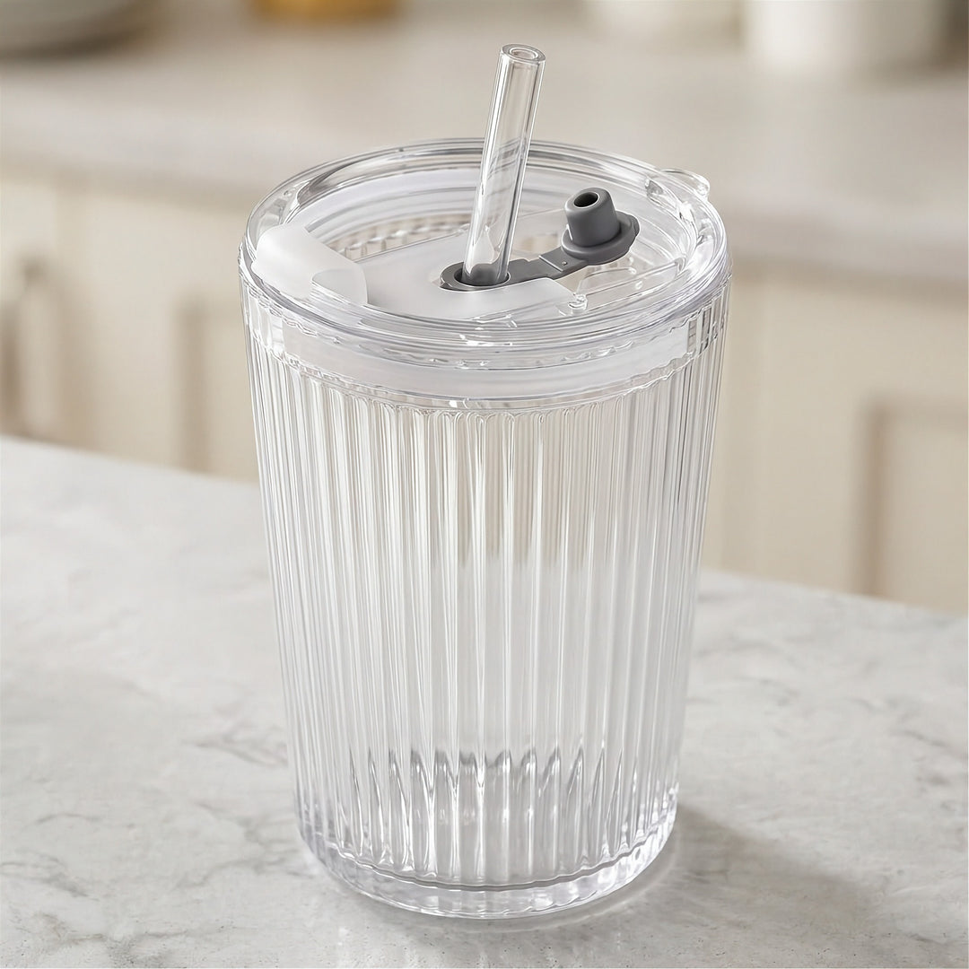 Clear ribbed tumbler with a transparent lid, straight clear straw, and gray drinking spout stands on a pale marble countertop.