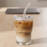 Clear ribbed tumbler holding a layered brown and white iced drink has a transparent lid and bent clear straw on a wooden table.