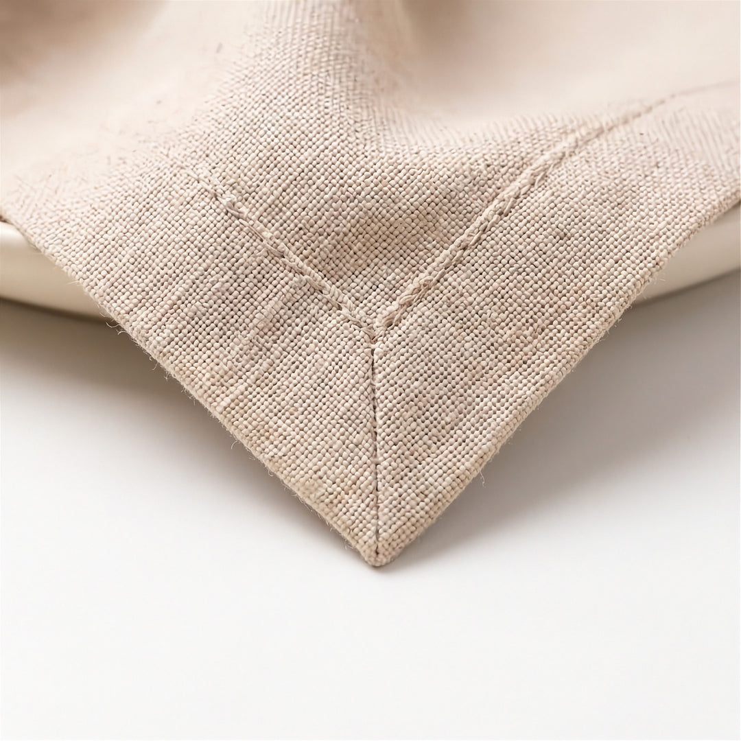 Close-up of a beige woven textile corner with visible stitching, resting on a white surface.