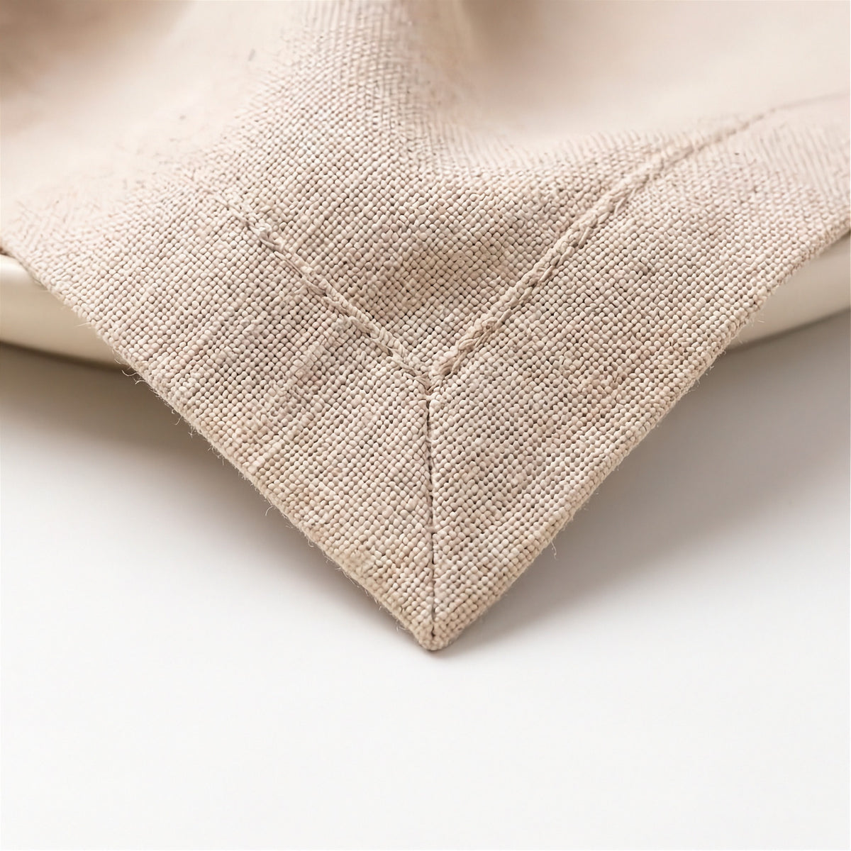 Close-up of a beige woven textile corner with visible stitching, resting on a white surface.