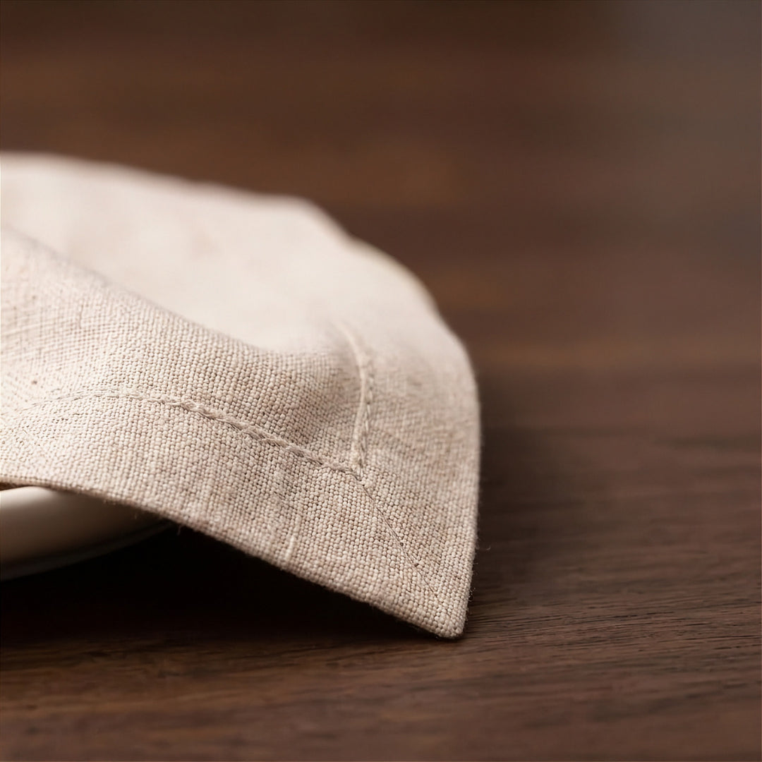 A close-up of a folded light beige linen napkin resting on a dark brown wooden table.