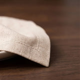 A close-up of a folded light beige linen napkin resting on a dark brown wooden table.