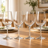 Four matching clear red wine glasses lined up on a dining table set with plates