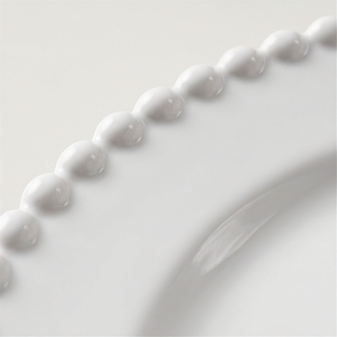 Close-up of a glossy white ceramic plate featuring a decorative beaded border and a curved rim.