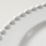Close-up of a glossy white ceramic plate featuring a decorative beaded border and a curved rim.