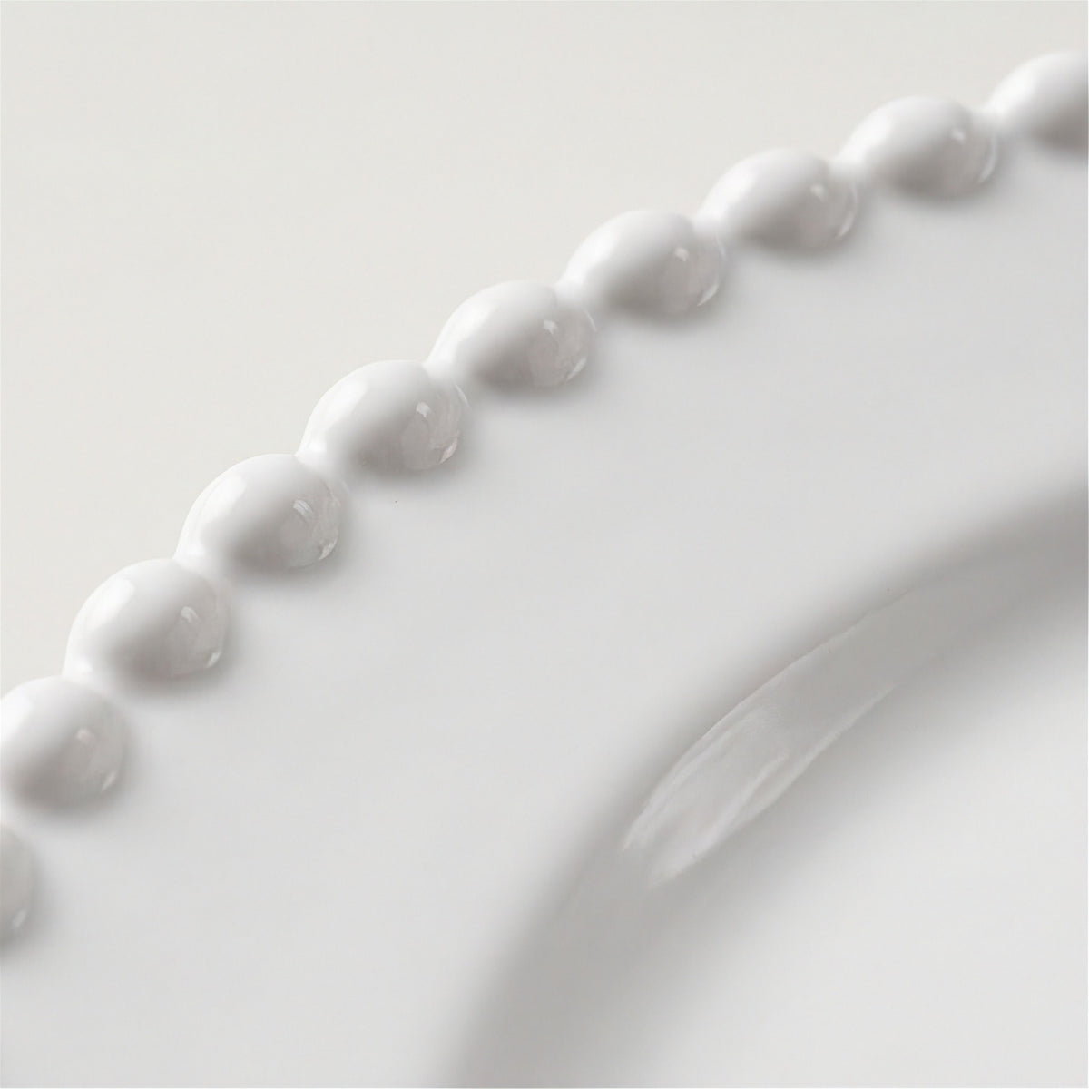 Close-up of a glossy white ceramic plate featuring a decorative beaded border and a curved rim.
