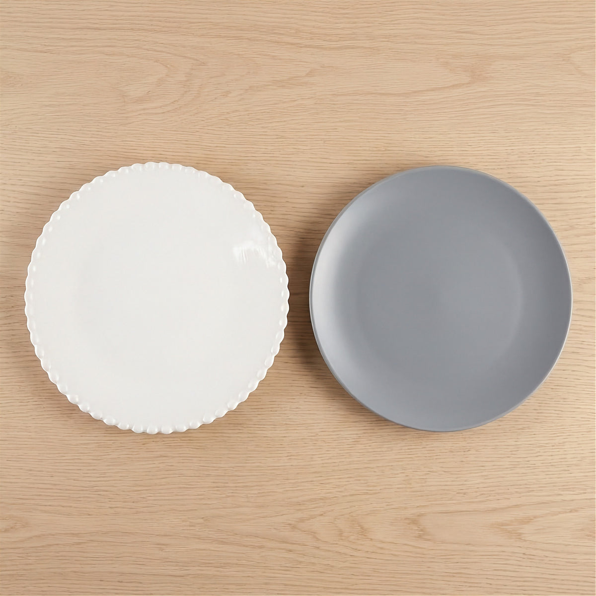 A white beaded-rim plate and a smooth gray round plate sit side by side on a light wooden surface.