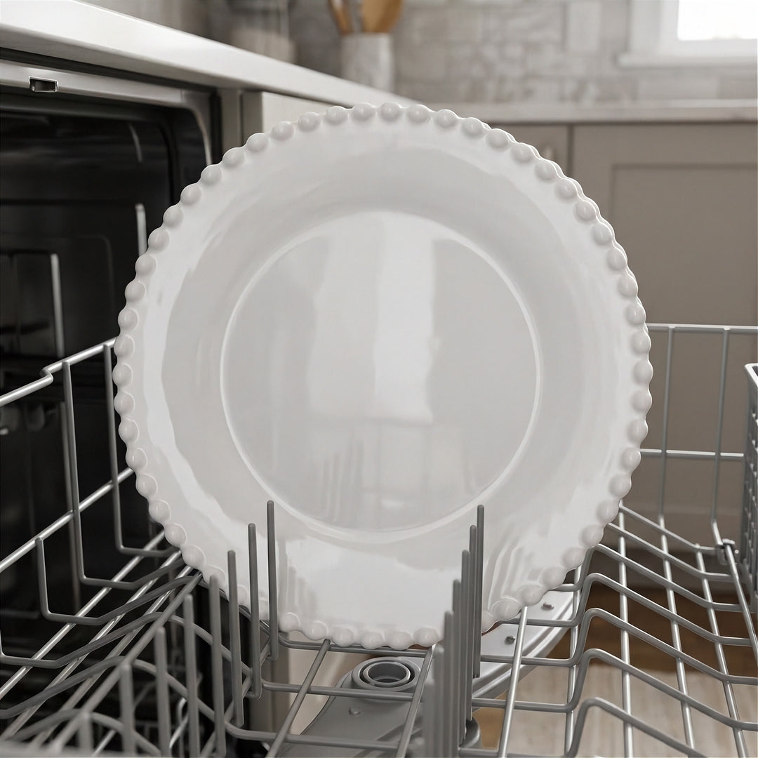 White plate with a beaded rim stands upright in a gray dishwasher rack, with kitchen cabinets in the background.