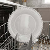 White plate with a beaded rim stands upright in a gray dishwasher rack, with kitchen cabinets in the background.