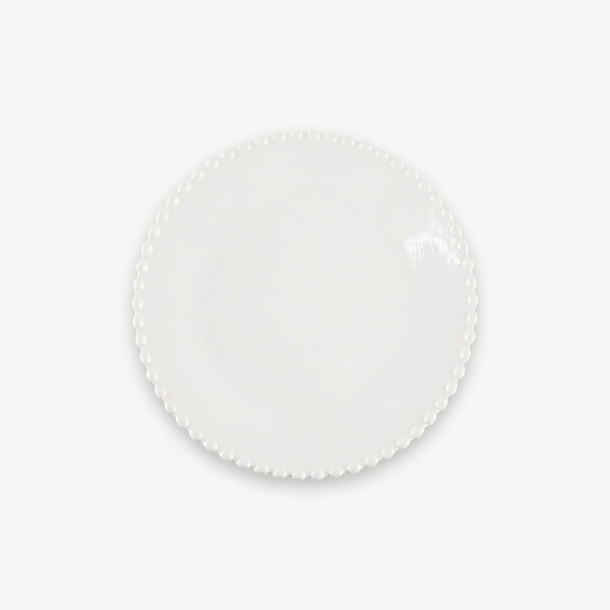 A white round plate with a glossy surface and beaded edge sits centered against a plain white background.