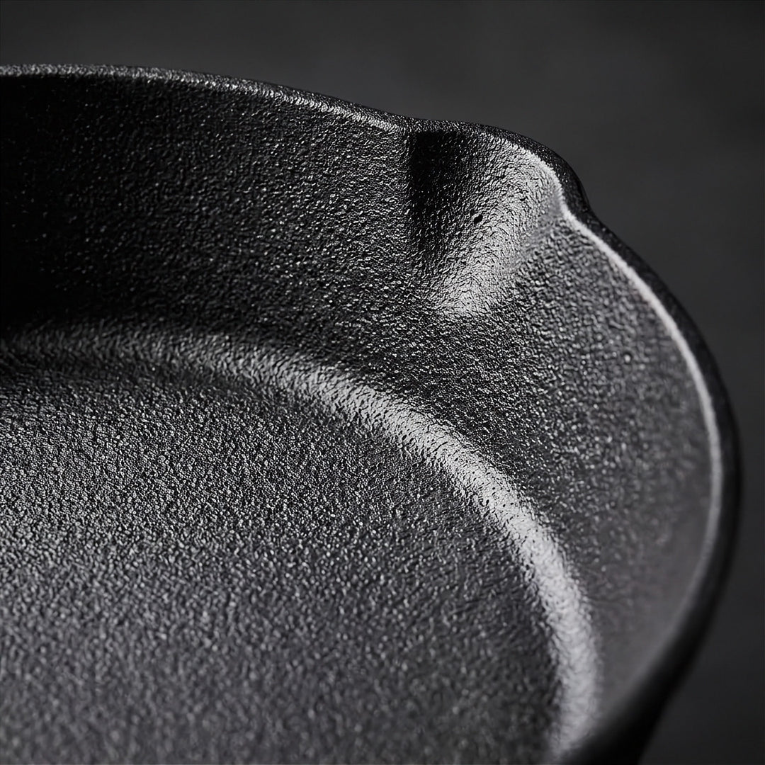 Close-up of a black cast iron skillet showing the textured interior rim and deep curve against a dark background.