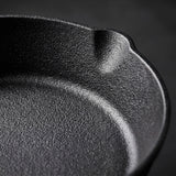 Close-up of a black cast iron skillet showing the textured interior rim and deep curve against a dark background.