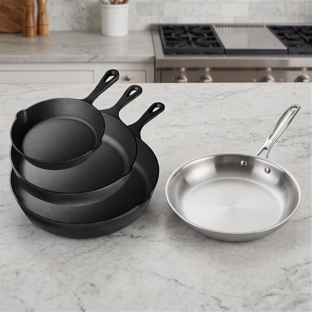 Three nested black cast iron skillets stand beside a silver frying pan on a pale kitchen countertop.