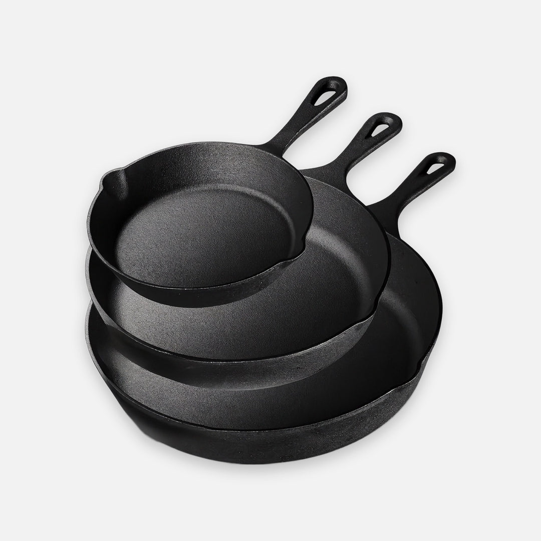 Three nested black cast iron skillets sit against a light background with their hanging handles pointing upward.
