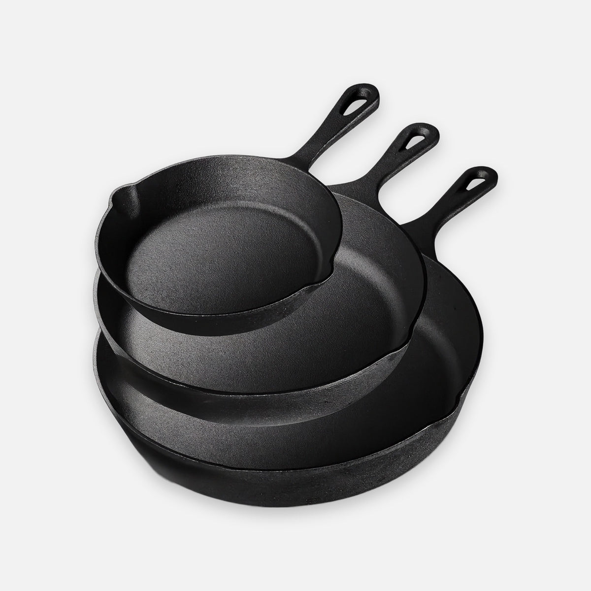 Three nested black cast iron skillets sit against a light background with their hanging handles pointing upward.
