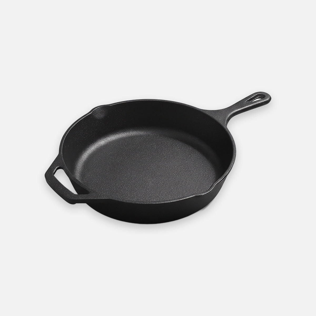A black cast iron skillet with a long handle, helper handle, and pouring spouts sits against a light background.
